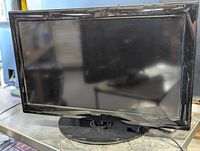 Front view of the black Coby 32-inch TFT LCD TV on circular stand showing reflective screen and frame.