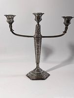 Front view of the ornate three-arm silver plated candelabra on white background