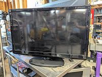 Front angle view of Dynex 40-inch digital TV on black stand, screen off but reflecting surroundings.