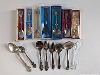 Full lot of 15 miniature collector spoons and 2 miniature forks including some in boxes, arranged in two rows showing overall variety and condition.