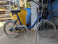 Left side view of blue vintage folding bicycle showing frame, seat, rear rack and tires.