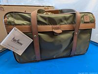 Front view of green ballistic nylon weekender bag with brown leather straps and Hartman leather tag, with attached tag showing brand authenticity.