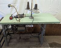Full view of the vintage Singer industrial serger sewing machine mounted on a metal frame table with attached lamp and thread stand with large cones of thread.