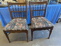 Front view of the two vintage wooden side chairs showing floral upholstered seats and classic turned spindle backs