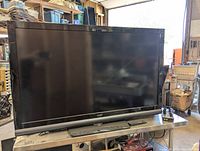 54-inch Vizio LCD TV powered on and displaying start-up screen on metal table in workshop environment.