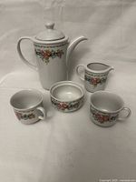 Coffee service items arranged on white background showing all pieces: coffee pot with lid, two cups, creamer jug, and sugar bowl without lid, all decorated with floral bouquet pattern