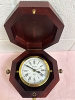 Open wooden octagonal box showing the clock inside with brass surround and Roman numeral dial.