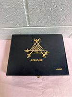 Closed black cigar box with gold Monte Cristo Afrique branding on top, 'Jambo' lettering on bottom right.