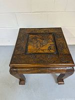 View of the wooden side table showing detailed Japanese-style carved tabletop comprising a landscape scene and floral border, with carved legs visible.