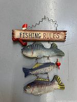 Full front view of the natural wood 'FISHING RULES' sign with three hanging painted wooden fish and fishing details.