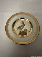 Full top view of the round decorative plate with pelican and gold rim, showing break and repair on the right side.