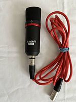 Front view of Scarlett Studio CM25 MkIII condenser microphone with attached red XLR cable coiled next to it, on white background.