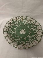Full top view of green porcelain serving dish with white grapevine design and gilding on edges and grape clusters