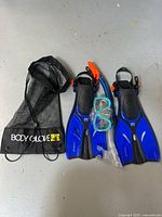 Full view of swimming set items laid out on floor showing fins, snorkel, face mask, and mesh carrying bag