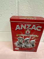 Front view of red vintage ANZAC oatmeal cookie tin with soldier illustrations and text.