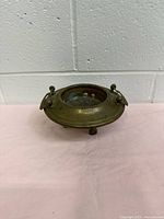 Front angle view of vintage brass and hammered copper candle holder with three legs and two loop handles, showing circular interior with copper and some patina.