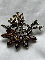 Close-up front angled view of the vintage brooch on white fabric background. Shows multicolored rhinestones and silver-tone metal detail.