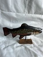 Side view of the carved wooden trout fish sculpture on a wooden stand showing the full length and shape of the fish.