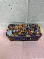 Front view of vintage collectible tin box showing detailed lid artwork featuring a teddy bear and vintage memorabilia.