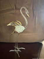 Front and side view of the vintage glass flamingo figurine showing clear glass body, textured midsection, and gold accents on wings and beak.