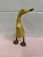 Front and side views of the hand carved wooden duck/goose figurine standing on two legs, pale creamy yellow with dark feet and beak, showing condition and details.