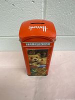 Front view of the red tin shaped like a London telephone booth showing teddy bear illustration and "TELEPHONE" top label.