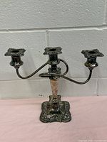 Front view of vintage heavy silver plated 3 candle candlestick showing three ornate candle sockets and curved arms.