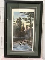 Full view of the framed vintage print showing the image of ducks on a lake with pine trees. Frame is wooden and dark, matting is green with white borders.