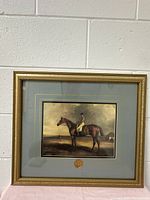Full view of vintage horse print framed in gold wooden frame with grey mat and medallion.