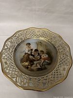 Full view of scalloped porcelain plate showing ornate gold lattice edge and central painted scene of three children.