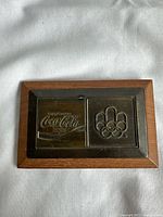 Front view of the vintage Coca-Cola tin sign on wooden base showing the embossed logos.