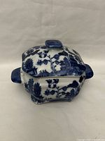Closed butter or sauce plate with lid showing blue and white Japanese pattern with nature scenes and blue handles.