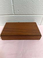 Closed view of rectangular wooden cigarette box on a fabric surface with visible wood grain and carved edges.