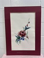 Full view of watercolor floral drawing with visible flowers and leaves on textured paper with maroon mat board border.