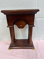 Front view of wooden watch case showing columns, curved center insert, brass feet, and side profile