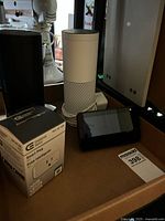 Group shot showing white Echo, boxed smart plug, Echo Show display, glimpse of black Echo