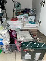 Overall view of lot under sink showing stacked wet wipes, Lacoste gift set, clear bin with sanitizers and basket of toiletries