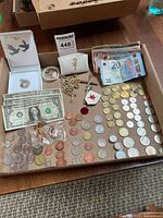 Overview of tray containing coins, banknotes, medals, rosary, pin, pouch