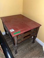 Three-quarter view of end table showing red top, carved legs, side accents