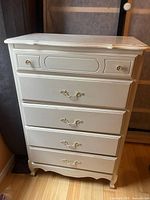Front view of off-white five-drawer tall chest with ornate pulls and scalloped base