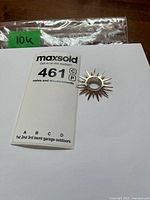 Front view of 10K gold sunburst pendant beside lot tag