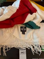 Close-up of blanket showing red and green stripes, white background, fringe, and maker’s label