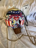Front view of hot-air-balloon shoulder bag showing print, basket base, chain strap and tag