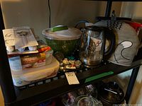 Shelf with salad spinner, stovetop kettle under cozy, spice rack, tea balls, plastic containers