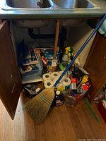 Under-sink cabinet showing cleaning products, garbage bags, foil, spray bottles, plastic bin