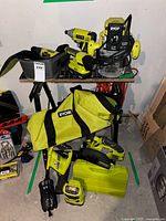 Group view of multiple Ryobi tools on stand with bags, charger and accessory cases