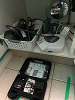 Shelf view showing hair dryer, curling iron in basket, mirror, bottles, white device and closed TENS case