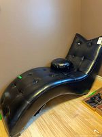 Full view of black faux leather tufted curved chaise lounge with round pillow