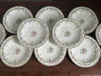 Top view of 10 porcelain bowls arranged closely on a wooden surface, showing floral center and rim pattern with gold detailing.