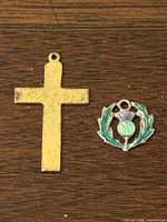 Front view of 10K gold crucifix next to sterling silver thistle pendant on wood background